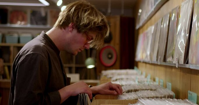 A stylish hipster man chooses vinyl records in a music store as a gift for a music collection. A DJ buys music for a party. A fashionable guy is looking for music on vinyl records in a vintage store