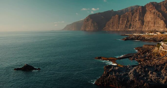 Natural ocean swimming pool in Tenerife Canary Islands. Charco de Isla Cangrejo. Gorgeous view to the Los Gigantes cliffs at sunset orange light.