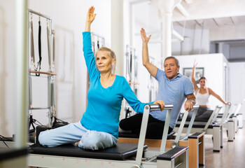 Elderly woman performing toning Pilates exercise for arms during group class in rehabilitation center
