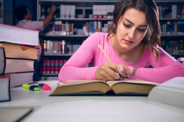 Young, beautiful student girl who studies at the library and writes notes. The girl is studying and preparing for the exam. Empty space for advertisement and slogan text