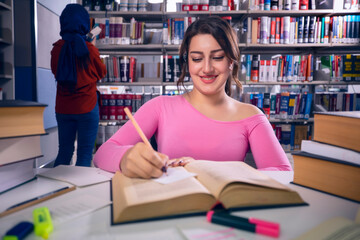 Young, beautiful student girl who studies at the library and writes notes. The girl is studying and preparing for the exam.