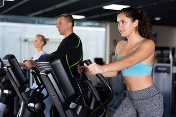 Active young woman training at elliptical machine in gym