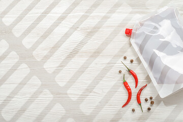 Ketchup in blank white doypack bag with spice on white wooden background. Top view of stand-up pouch.