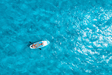 Aerial view of sup board with people in blue sea at sunny summer day. Floating canoe in transparent azure water. Sardinia island, Italy. Tropical landscape. Kayak. Active travel. Top drone view. Sport