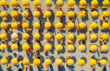Aerial view of yellow umbrellas on sandy beach at sunset in summer in Sardinia, Italy. Tropical colorful landscape. Travel and vacation background. Top down view from drone. Tropical pattern. Concept - obrazy, fototapety, plakaty