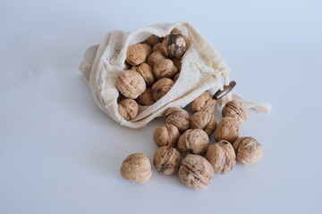 Shelled walnuts falling from a white cloth bag on a white background. 
