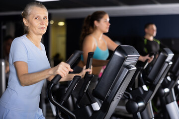 Fototapeta na wymiar Mature woman exercising on an elliptical trainer in the gym
