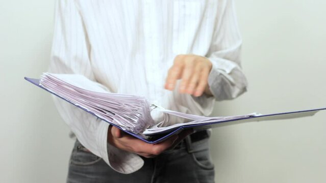 Video of a young man, obviously business man, student or teacher on white background holding an office folder with documents in his hands and turning pages while reading it