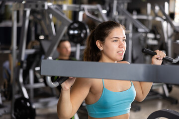 Sporty young woman using shoulder press machine in gym