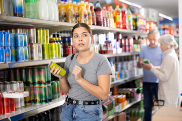 Young woman chooses carbonated drink in an aluminum can in the grocery section of a supermarket