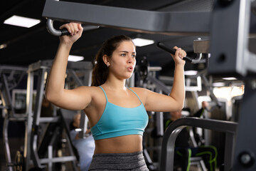 Fototapeta na wymiar Young woman trains her arm muscles using a simulator in the gym