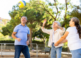 Positive multiracial friends of different ages throwing up a volleyball ball in a circle on the...