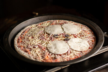 The pizza goes to the oven. Pizza with big circles of cheese. Home cooking.