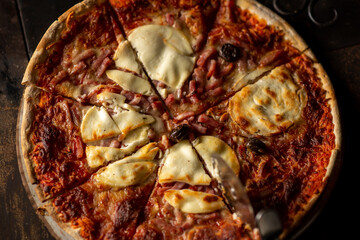 Freshly cooked pizza. Top view. Cut into pieces. Dark background. Close-up.