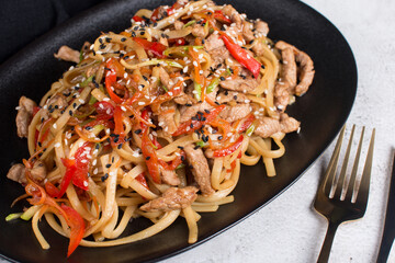 spaghetti with vegetables sauce and meat on a black plate. the concept of the restaurant serving dishes wok