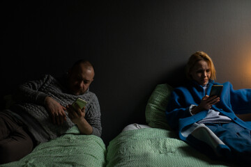 Fototapeta premium Two bored spouses. Indifference in a couple. Everyone has their own interests. Husband and wife in different beds.