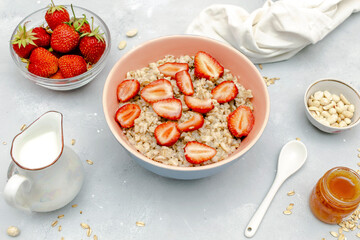 Oatmeal porridge with summer strawberries berries. Porridge oats in bowl with honey,milk,nuts. Healthy food breakfast,lifestyle,dieting, proper nutrition. Top view flat lay on gray table background