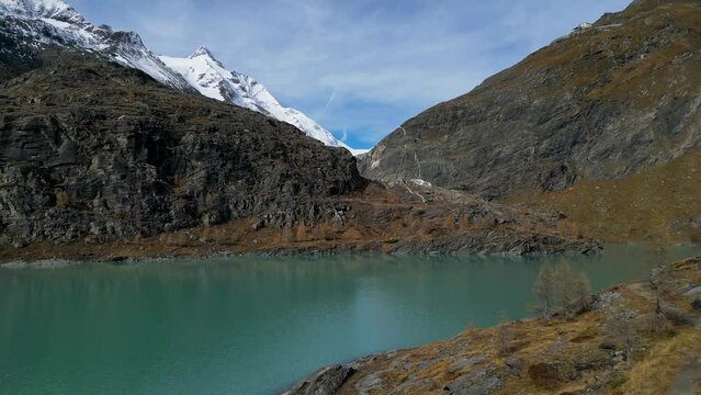 Margaritze artifical lake with Grossglockner Summit in Hohe Tauern in Alps with glowing larch trees in autumn, Austria