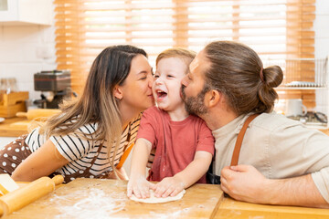 Obraz na płótnie Canvas Caucasian father and mother teaching baby son kneading dough on kitchen counter at home. Parents and child boy kid enjoy and fun indoors activity cooking pizza together. Family relationship concept.
