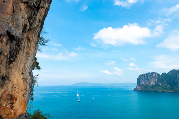 Fototapeta premium Landscape of the Ocean with tropical island mountain peak in Krabi prefecture, Thailand in sunny day. Beautiful nature of blue sea with tourist yacht boat passing the beach on summer holiday vacation.