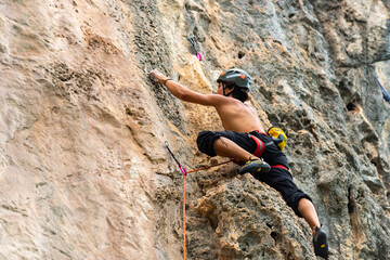 Young Asian man climber climbing on rocky coastline at tropical island in sunny day. Handsome guy enjoy outdoor active lifestyle and extreme sport training mountain climbing on summer holiday vacation