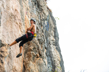 Young Asian man climber climbing on rocky coastline at tropical island in sunny day. Handsome guy enjoy outdoor active lifestyle and extreme sport training mountain climbing on summer holiday vacation