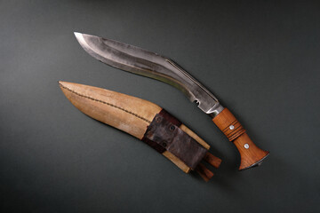 An ancient curved kukri knife with a sheath on a dark background