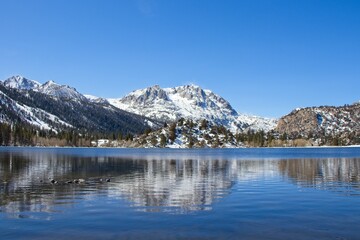 Fototapeta na wymiar Snow tops the Sierra Nevada Mountains from the crystal clear waters of June Lake, which sits at the bottom of the mountain range's steep eastern escarpment