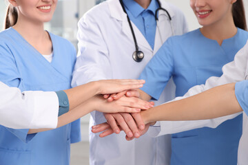 Team of medical doctors putting hands together indoors, closeup