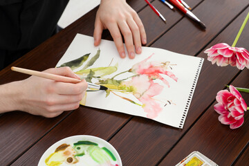 Obraz na płótnie Canvas Woman painting flowers with watercolor at wooden table, closeup. Creative artwork