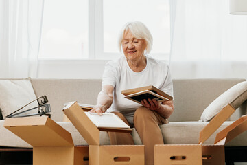 elderly woman sits on a sofa at home with boxes. collecting things with memories albums with photos...