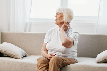 Elderly woman severe neck pain sitting on the sofa, health problems in old age, poor quality of life.