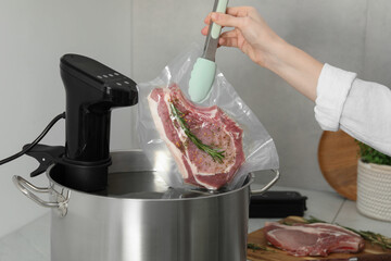 Woman putting vacuum packed meat into pot with sous vide cooker in kitchen, closeup. Thermal...