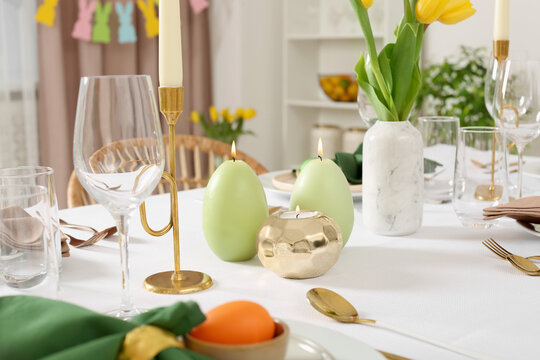 Festive Easter table setting with painted eggs, burning candles and yellow tulips indoors