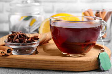 Tea bag in glass cup, anise stars and cinnamon sticks on light grey table, closeup