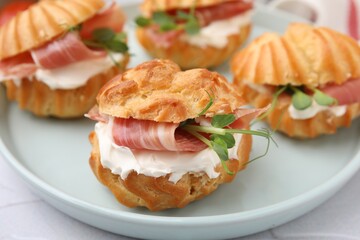 Delicious profiteroles with cream cheese and prosciutto on plate, closeup