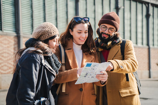 three tourist happy friends looking for directions on a map enjoying their weekend travel to new city, searching locations on the guide. Group of young people visiting Europe and planning the day