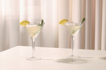 Elegant martini glasses with fresh cocktail, rosemary and lemon slices on white table indoors