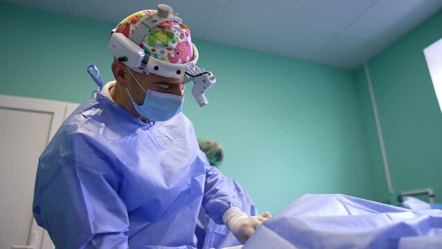 Surgeon wearing headlight working in surgery room. Doctor uses metal tool at operation on thyroid. Low angle view.