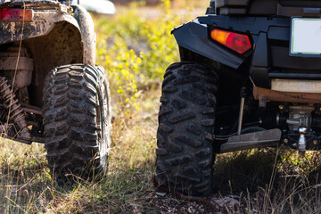 Obraz premium Close-up tail view of ATV quad bike on dirt country road. Dirty wheel of AWD all-terrain vehicle. Travel and adventure concept.