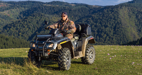 Fototapeta na wymiar A man driving a quad ATV motorcycle through beautiful meadow landscapes