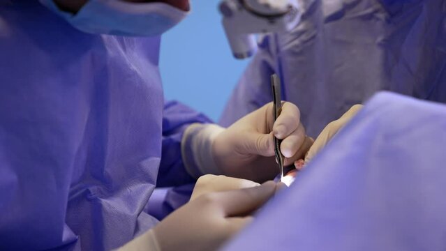 Operation on thyroid in modern clinics. Surgeon carefully uses forceps and scalpel lighting the operational spot with headlight.