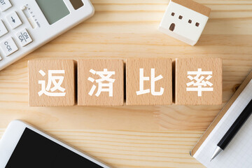 返済比率と書かれたブロック、電卓、家の模型、スマホ、ノート