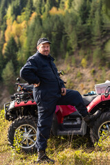 Fototapeta na wymiar A man in a forest area posing next to a quad and preparing for ride