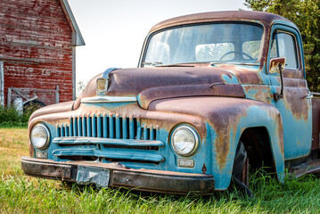 A vintage half ton pickup truck in front of a red barn on the Canadian prairies