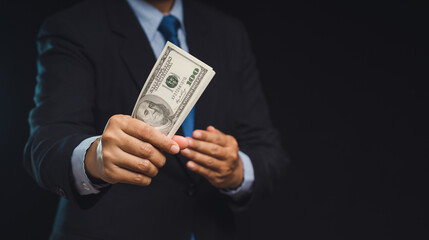 Businessman holding US dollar bills while standing on a black background