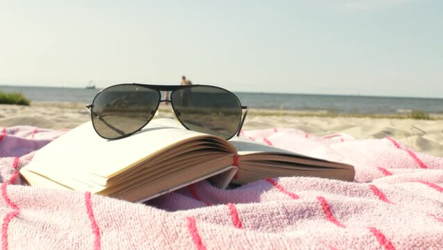 High quality video of father and son playing on the background near seashore, sunglasses and opened book are lying on the pink beach towel foreground