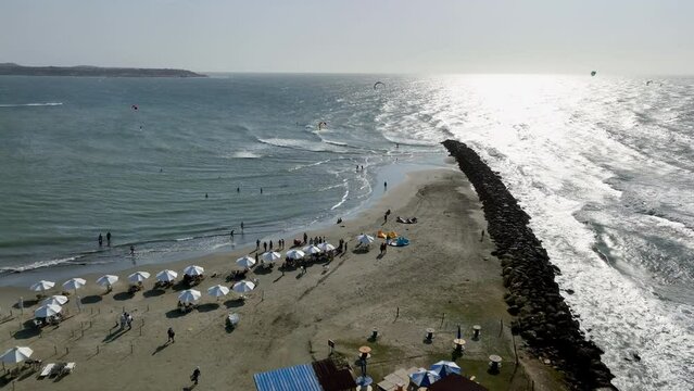 Drone shot over the a beach, toward parasailers on the coast of Cartagena, Colombia