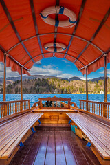 Bled, Slovenia - Traditional wooden red canvas roof Pletna boat at Lake Bled (Blejsko Jezero) on a sunny autumn day with Julian Alps and weekend house at background. Blue sky and clouds