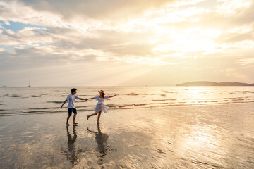 Young woman traveler holding man's hand and looking beautiful sunset on the beach, Couple on...